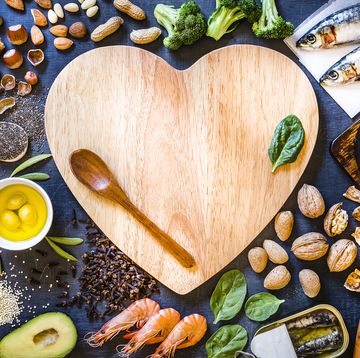 top view of wooden cutting board with a heart shape surrounded by an assortment of food rich in omega 3 like various kinds of nuts like hazelnuts, peanuts and almonds, canned and raw fish like salmon and sardine, some heaps of seeds like chia seeds, quinoa and flax seeds, some fruits like avocado and olives, vegetables like spinach and broccoli, and olive oil the cutting board has a wooden spoon and a spinach leaf but also has a useful copy space on top 
low key dslr photo taken with canon eos 6d mark ii and canon ef 24 105 mm f4l
