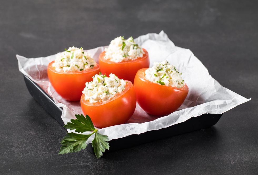tomatoes stuffed with cottage cheese with parsley on a serving plate on a dark gray background